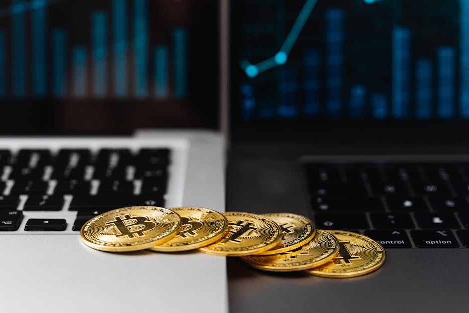 Gold bitcoins placed on laptop keyboards with digital financial graphs in the background.